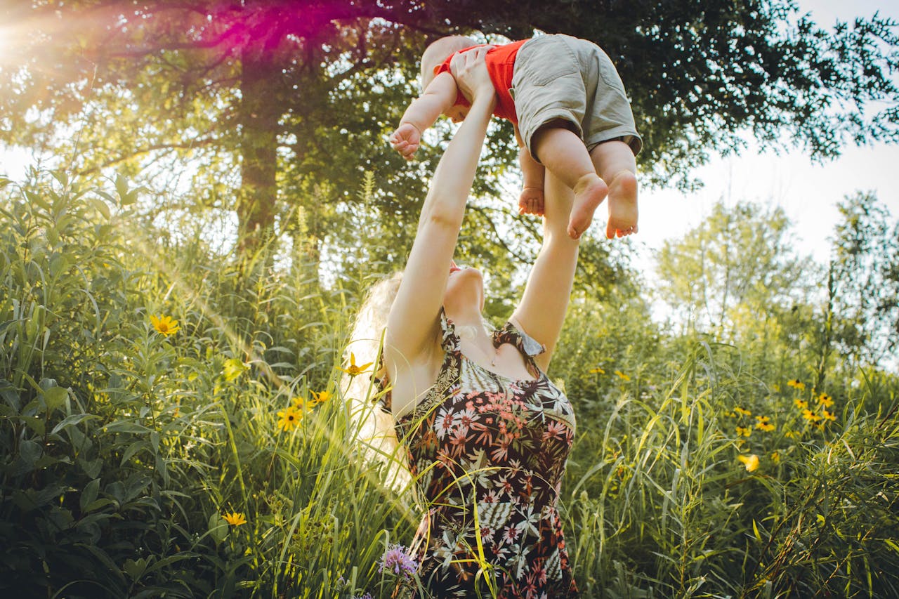 A joyful mother lifts her baby in a sunny summer meadow, capturing a moment of love and happiness.